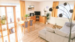 Un salon comprenant un canapé, une table à manger avec des chaises, un téléviseur et une bibliothèque.