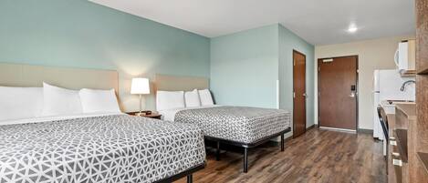 A hotel room with two beds, a wooden floor, a kitchenette, and a door leading to another room.