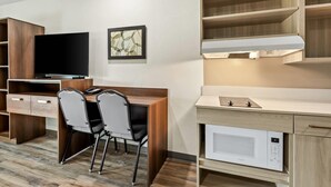 Una habitación de hotel moderna con un escritorio de madera, un televisor de pantalla plana, un microondas y una pequeña kitchenette.