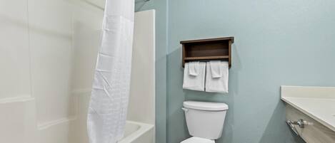 Un baño con bañera, inodoro y estante con toallas.