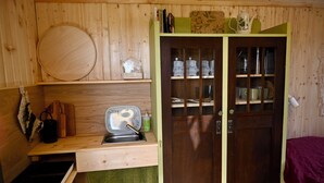 A compact kitchen with a sink, a microwave, and a small countertop. There is a wooden door with glass panels and a green shelf above it. - Bee wagon with fireplace & sauna can be used all year round in the natural garden (Dargun)