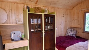A wooden cabin interior with a bed, a small kitchenette, and a wardrobe with glass doors. - Bee wagon with fireplace & sauna can be used all year round in the natural garden (Dargun)