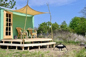 A green wooden structure with a porch, wicker chairs, and a barbecue grill. - Travel trailer with a fireplace and sauna, available year-round in a natural garden (Dargun)
