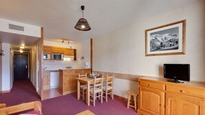 A compact room with a kitchenette, a dining area, and a television. - Cozy Retreat with Ski Access (Les Deux Alpes)