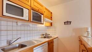A kitchen with wooden cabinets, a microwave, a stove, a sink, and a coffee maker. - Cozy Retreat with Ski Access (Les Deux Alpes)