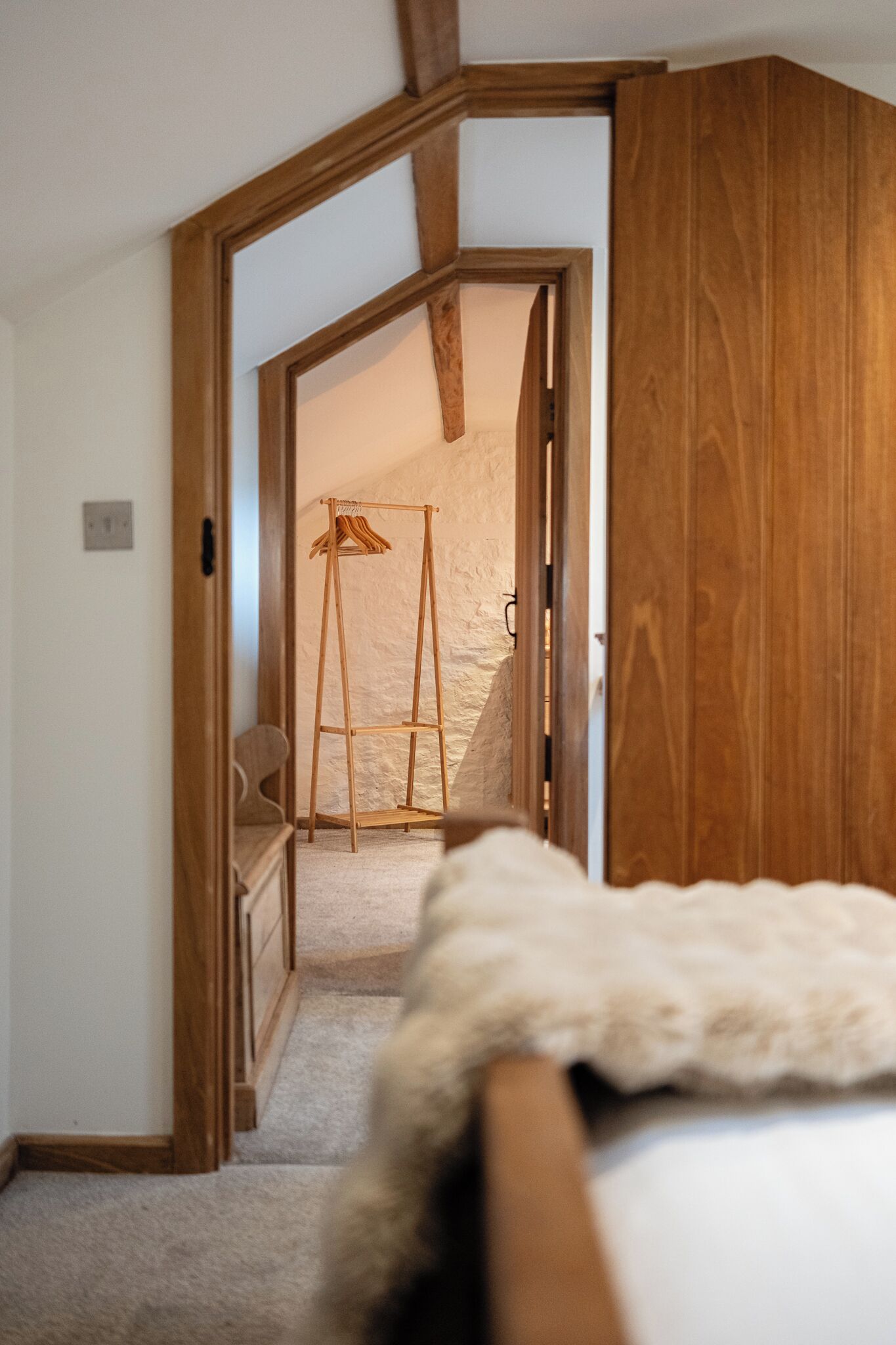 Un dormitorio con un armario de madera, una cama con cubrecama blanco y esponjoso, y una escalera de madera en la esquina.