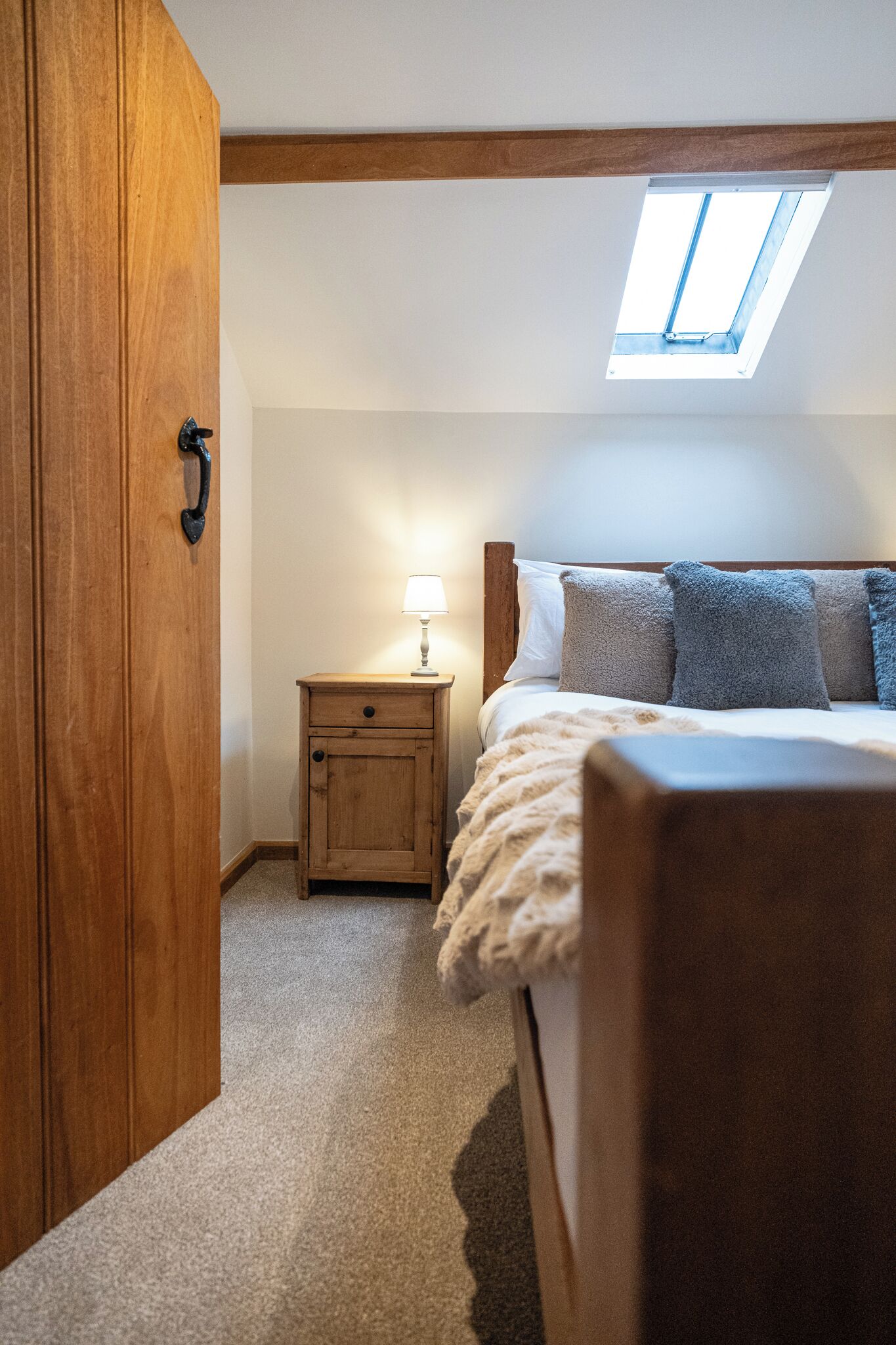 Un dormitorio con tragaluz, cama de madera, mesita de noche con lámpara y armario.
