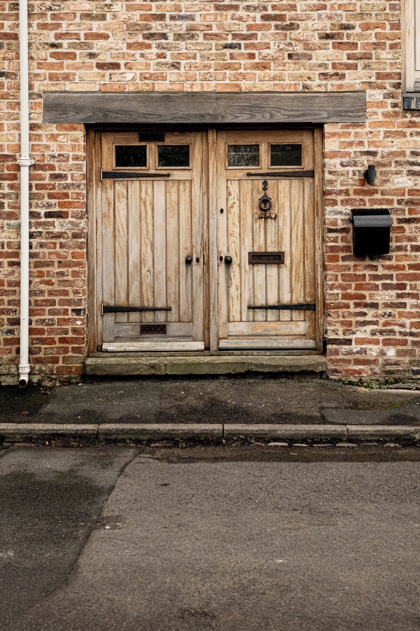 A wooden double door with a metal handle, set in a brick wall with a small step leading up to it.