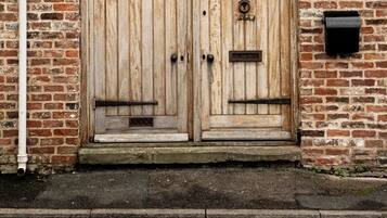 A wooden double door with a metal handle, set in a brick wall with a small step leading up to it.
