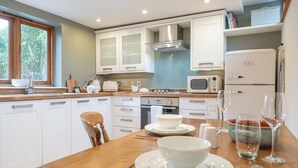 A modern kitchen with white cabinets, a wooden countertop, a built-in oven, a microwave, and a refrigerator. - Coach House - Lovely Home in Cheltenham (Cheltenham)
