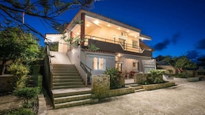 A two-story house with a stone staircase leading to the entrance, surrounded by greenery.