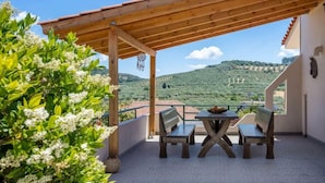 A covered patio with a table and benches, overlooking a hilly landscape.