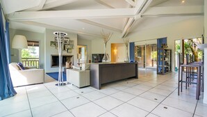 Amplia sala de estar con un sofá blanco grande, una mesa de centro moderna y un televisor de pantalla plana. Cuenta con una zona de comedor con barra y taburetes altos. La habitación tiene techos altos con vigas a la vista y ventanas grandes que permiten la entrada de luz natural.