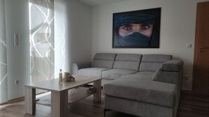 Una sala de estar moderna con un sofá gris, una mesa de centro de madera y un cuadro abstracto grande en la pared.