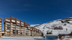 A multi-story hotel with balconies, a swimming pool, and a snowy mountain backdrop.