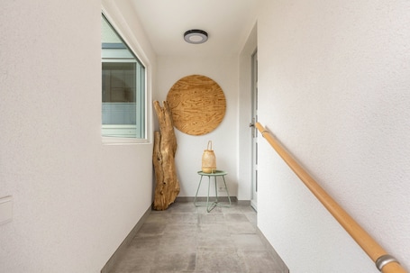 A hallway with a wooden floor, a round wall decoration, a wooden post, and a small table with a basket.. Holiday Home 'Höhe26' with Private Terrace, Garden, and Wi-Fi