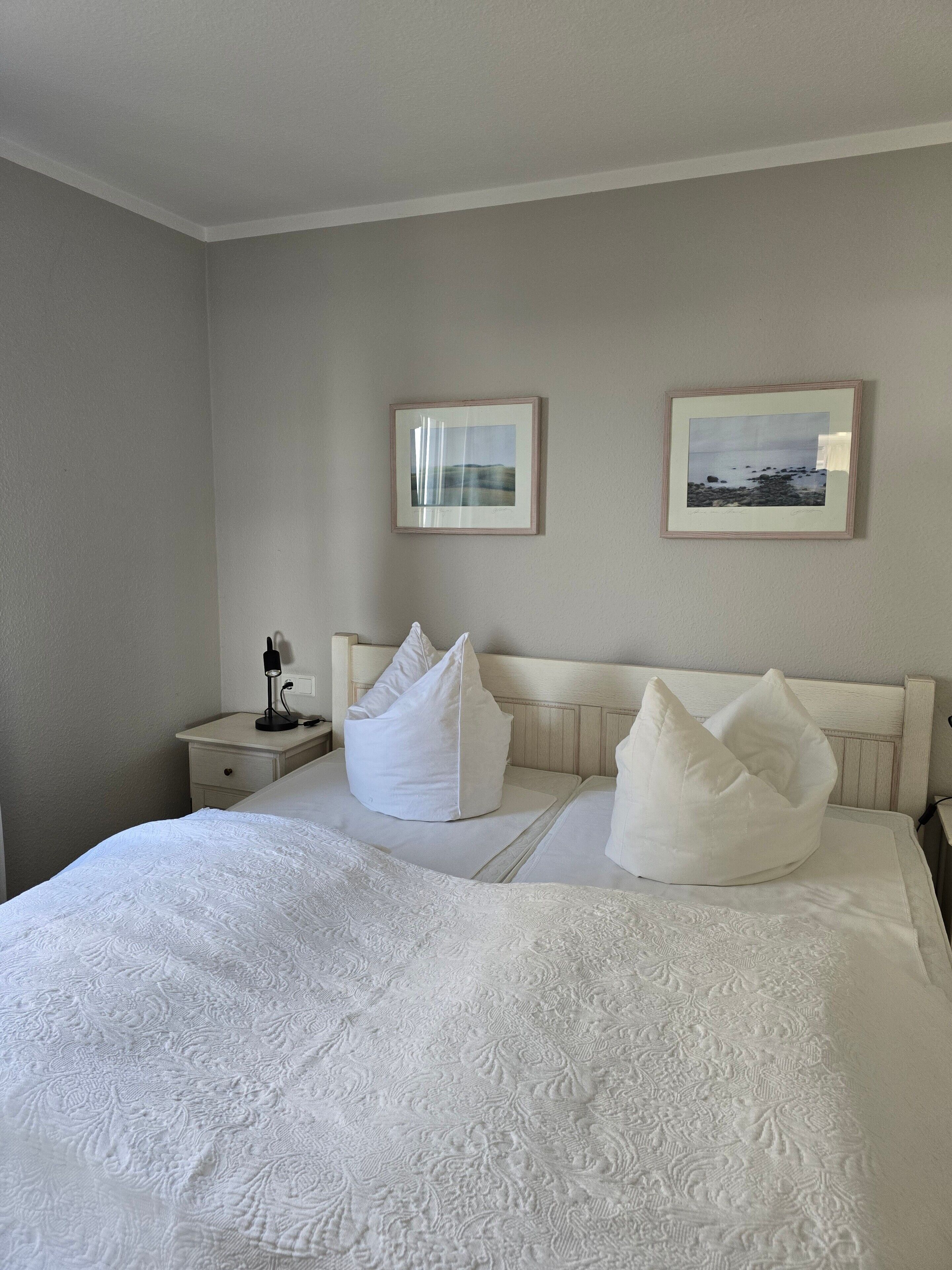 Un lit bien fait, recouvert d’une couvre-lit à motifs, avec deux oreillers blancs, une lampe de chevet et deux tableaux encadrés accrochés au mur.