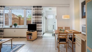 Ein modernes Wohnzimmer mit Fernseher, Esstisch, Stühlen und einer Küchenzeile mit Schränken und einem Fenster.