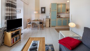 Ein Wohnzimmer mit Fernseher, Bücherregal, Esstisch und einer Couch.