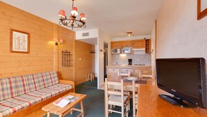 Ein gemütliches Zimmer mit einer Holzdirektiva, einem kleinen Tisch, einem Fernseher und einer Küchenzeile im Hintergrund.