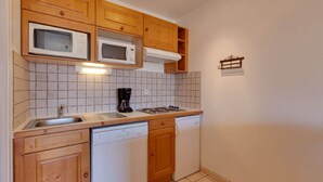 Eine kompakte Küche mit Holzausstattung, einer Mikrowelle, einer Kaffeemaschine, einem Geschirrspüler und einer gefliesten Spritzschutzwand.