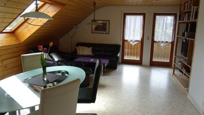 A loft-style room with a dining table, chairs, a sofa, a bookshelf, and a ceiling fan. - Apartment 'Zerlaut' with Balcony and Wi-Fi (Langenargen)