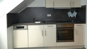 A kitchen with a dishwasher, oven, and stove, with light-colored cabinets and a black countertop. - Apartment 'Zerlaut' with Balcony and Wi-Fi (Langenargen)
