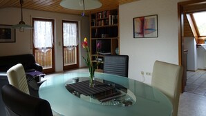 A dining area with a glass table, chairs, a vase with flowers, a bookshelf, and a painting on the wall. - Apartment 'Zerlaut' with Balcony and Wi-Fi (Langenargen)