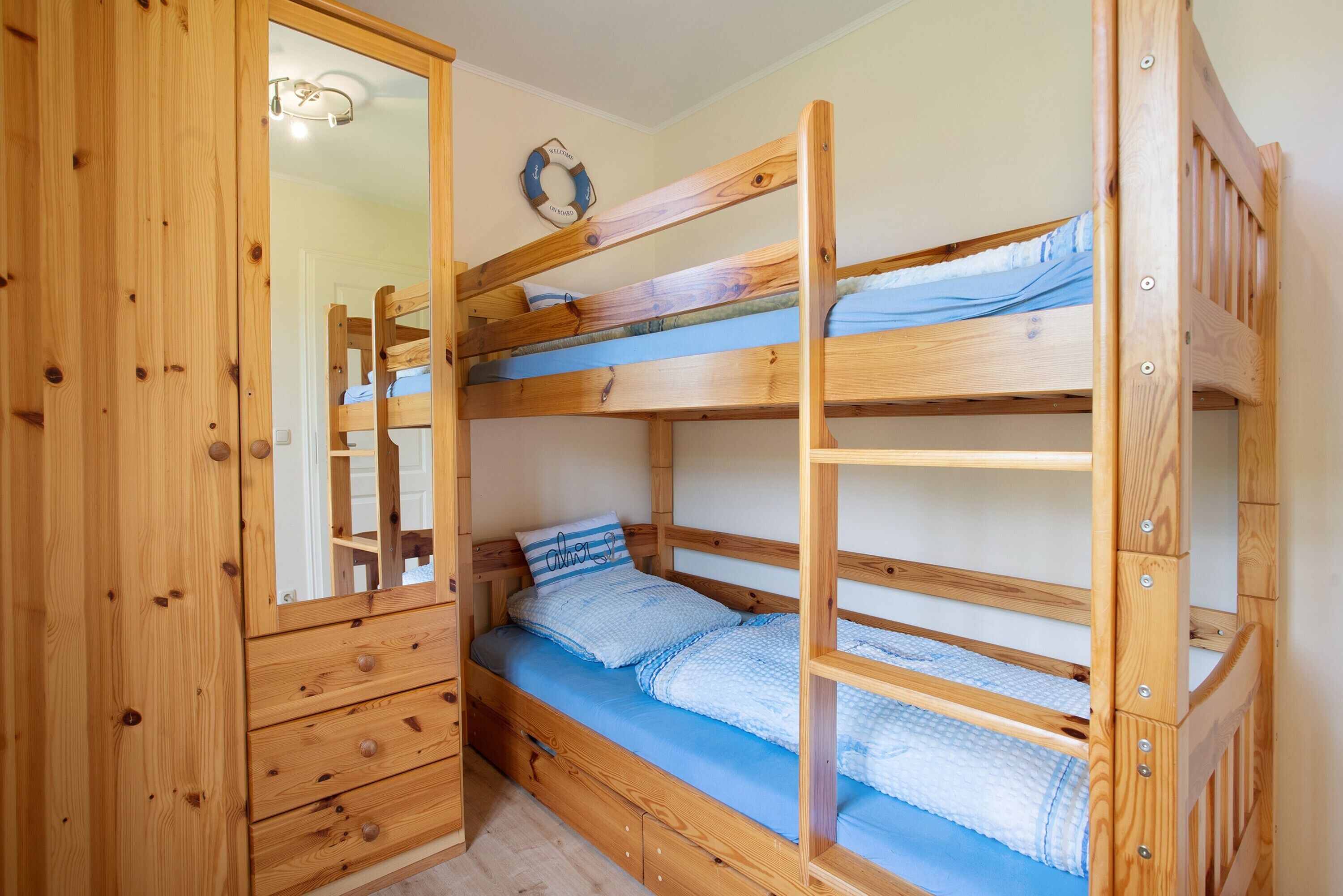 Une chambre avec un lit superposé, une armoire en bois, un miroir et un élément décoratif mural.