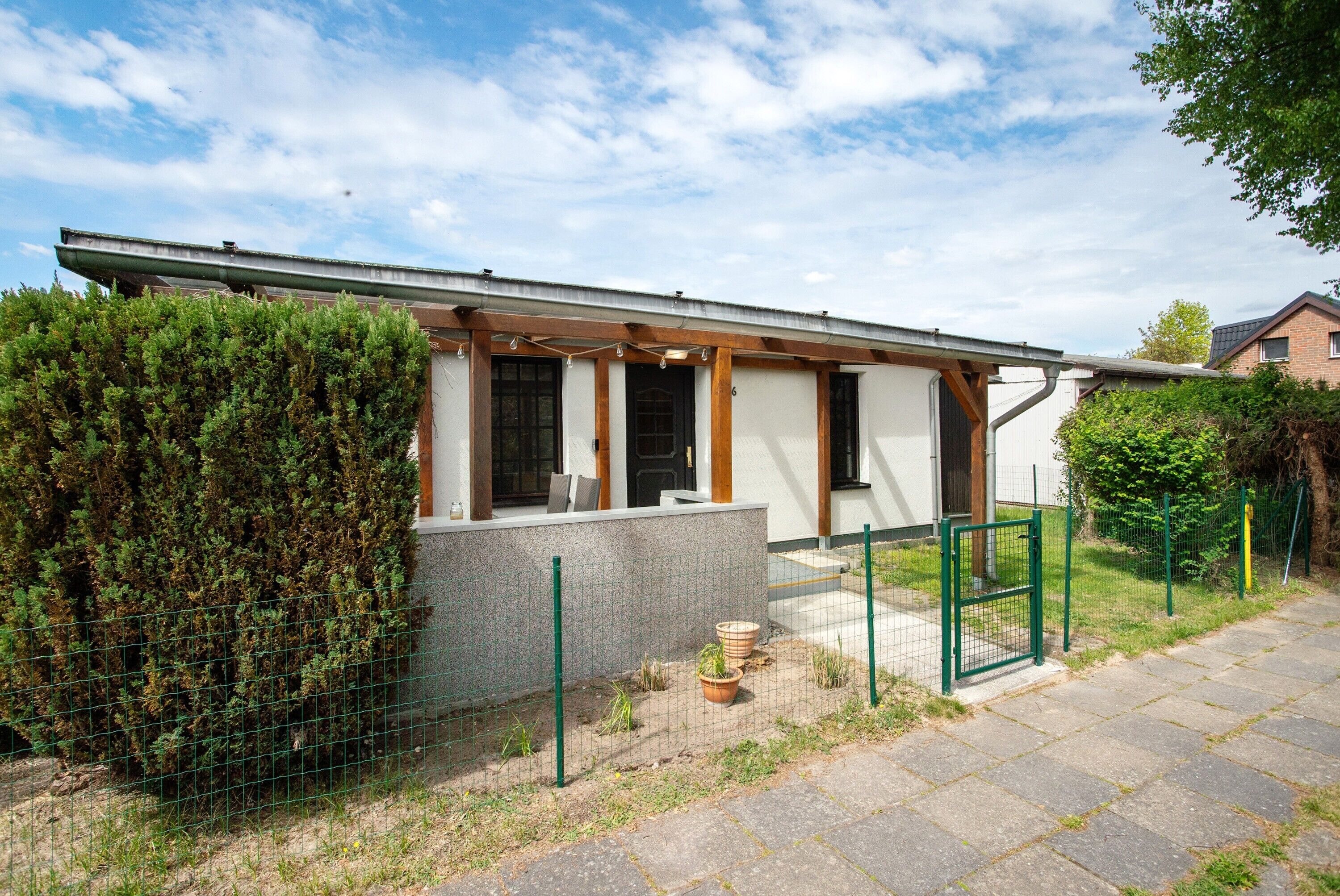 Ein modernes Einfamilienhaus mit überdachter Veranda, einem eingezäunten Garten und einer gepflasterten Auffahrt.