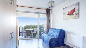 Un balcon avec un canapé bleu, une table avec des chaises et un tableau accroché au mur.