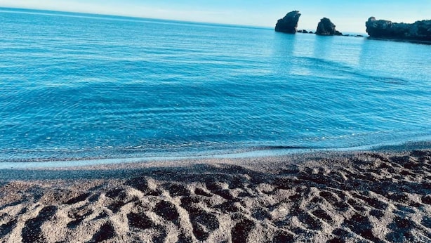 Une plage avec une eau d’un bleu limpide et des formations rocheuses visibles au loin.