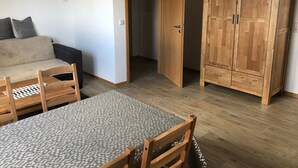 A room with a sofa, a dining table with chairs, a wooden wardrobe, and a door leading to another room. - Apartment 'Orthsee 2' with Shared Terrace and Wi-Fi (Hohen Wangelin)