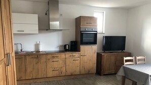 A compact kitchen with wooden cabinets, a stainless steel range hood, a built-in oven, a coffee maker, and a television on a wooden cabinet. - Apartment 'Orthsee 2' with Shared Terrace and Wi-Fi (Hohen Wangelin)