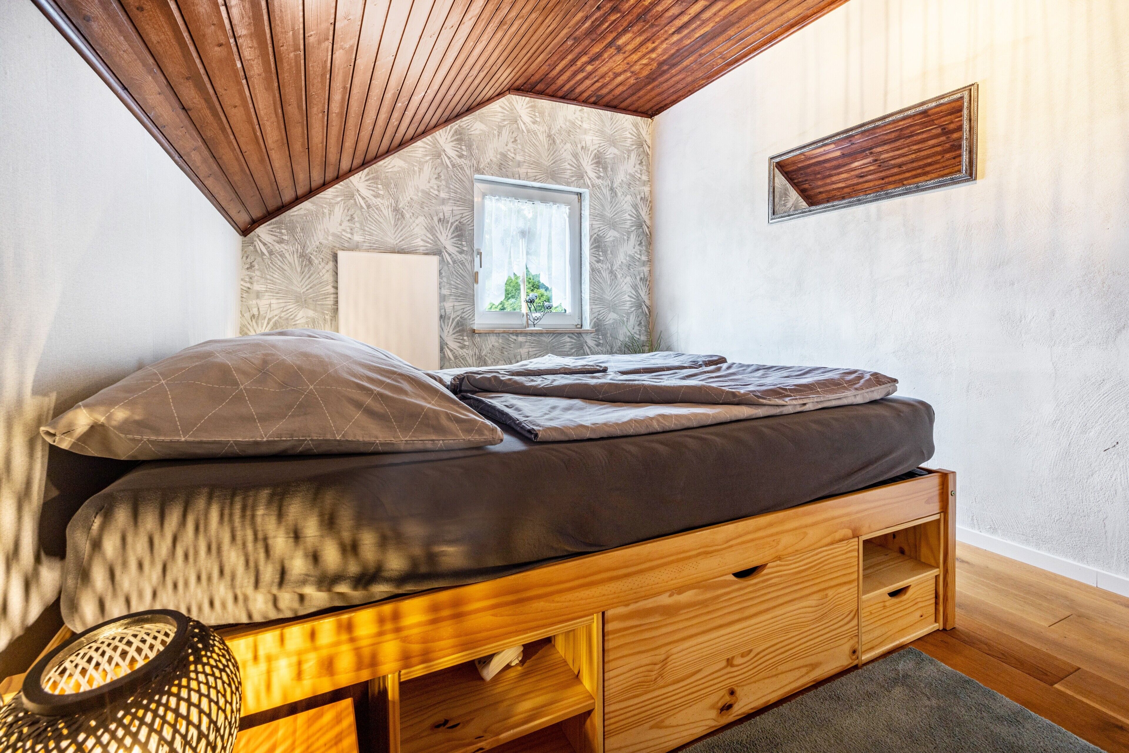 Une chambre de style « loft », avec un plafond en pente, une fenêtre offrant une belle vue, un lit doté de tiroirs de rangement et une petite table avec une lampe.