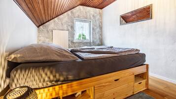 Une chambre de style « loft », avec un plafond en pente, une fenêtre offrant une belle vue, un lit doté de tiroirs de rangement et une petite table avec une lampe.