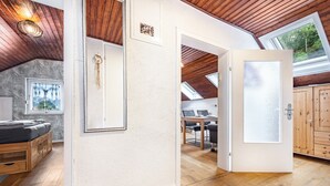 Een kamer met een schuine kap, houten balken, een bed, een bureau en uitzicht door een deur.
