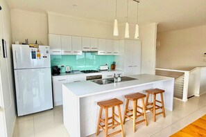 A modern kitchen with white cabinetry, a large island with bar stools, and pendant lighting.