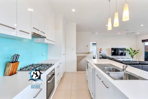 A modern kitchen with white cabinets, a gas stove, a built-in oven, a large island with a sink, and pendant lighting.