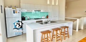 A modern kitchen with white cabinets, a central island with stools, and a refrigerator with a security lock.