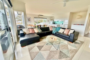 A modern living room with a sectional sofa, a glass coffee table, and a kitchen in the background.