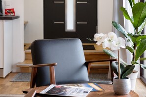 Una habitación moderna con una butaca de cuero oscura, una mesa de madera con una revista, una planta en maceta y vistas de una puerta negra.