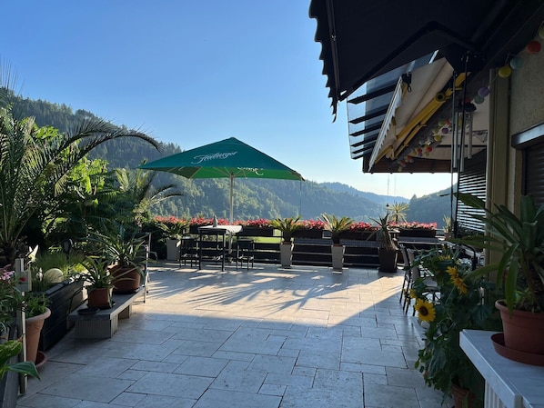 An outdoor patio with a green umbrella, potted plants, and a view of a mountain.