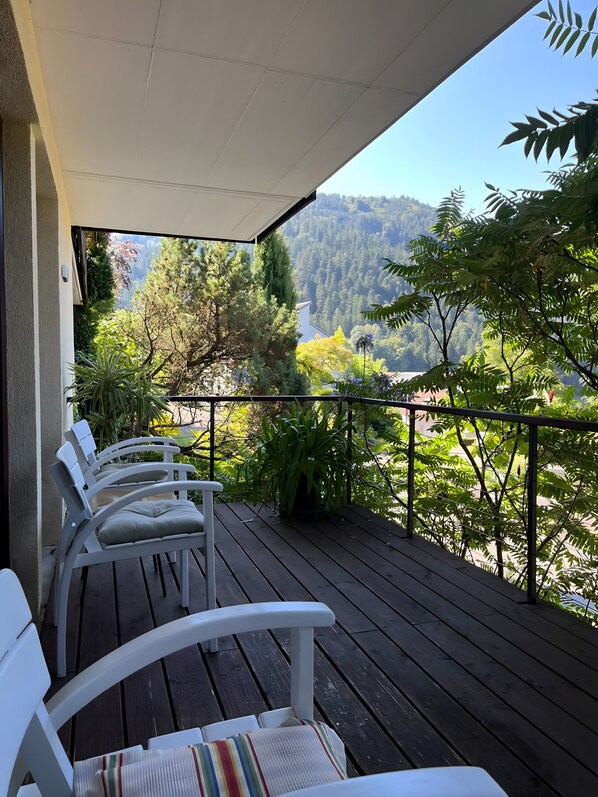 Una terraza de madera con sillas blancas y vistas a una ladera boscosa.