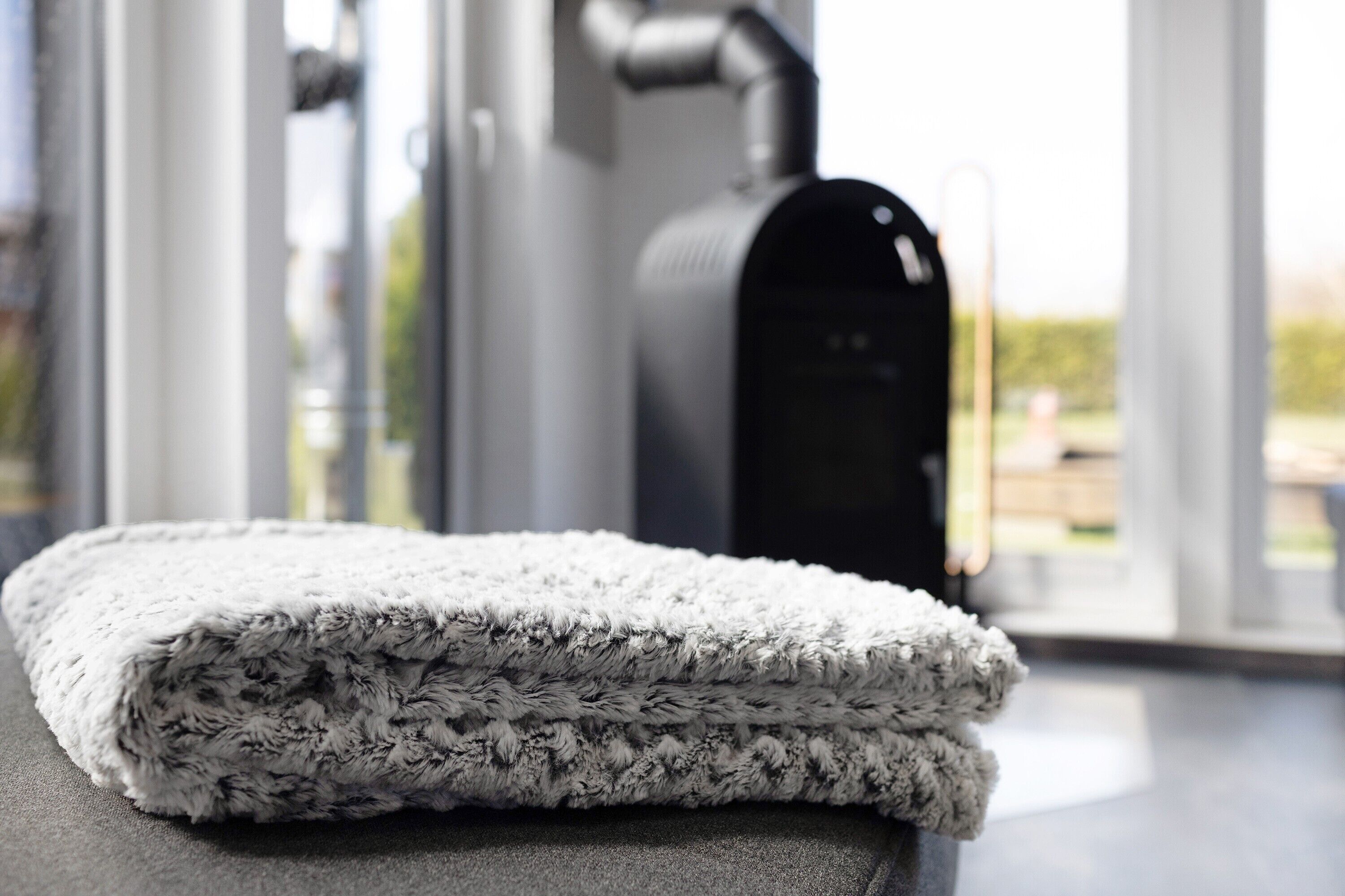 A folded, textured blanket on a dark surface with a blurred background featuring a window and a piece of exercise equipment.