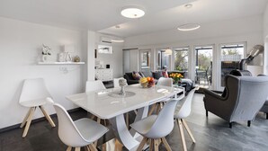 A modern dining area with a white table, grey and white chairs, and a grey sofa. - Holiday Home 'Happy-Nest' sauna pool air conditioning Wi-Fi fireplace barbecue (Oberkrämer)