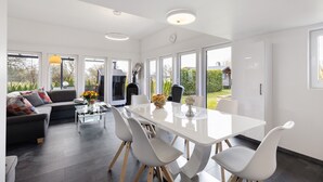 A modern living room with a sofa, dining table, chairs, and large windows. - Holiday Home 'Happy-Nest' sauna pool air conditioning Wi-Fi fireplace barbecue (Oberkrämer)