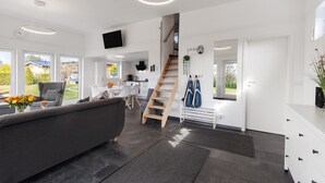 A modern living room with a grey sofa, a wooden ladder, and a staircase leading to a kitchen area. - Holiday Home 'Happy-Nest' sauna pool air conditioning Wi-Fi fireplace barbecue (Oberkrämer)