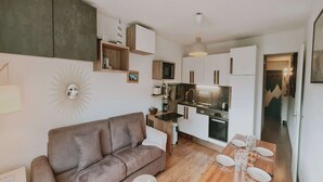 Ein kompakter Wohnbereich mit Sofa, Esstisch, Küchenzeile und kleinem Fernseher.