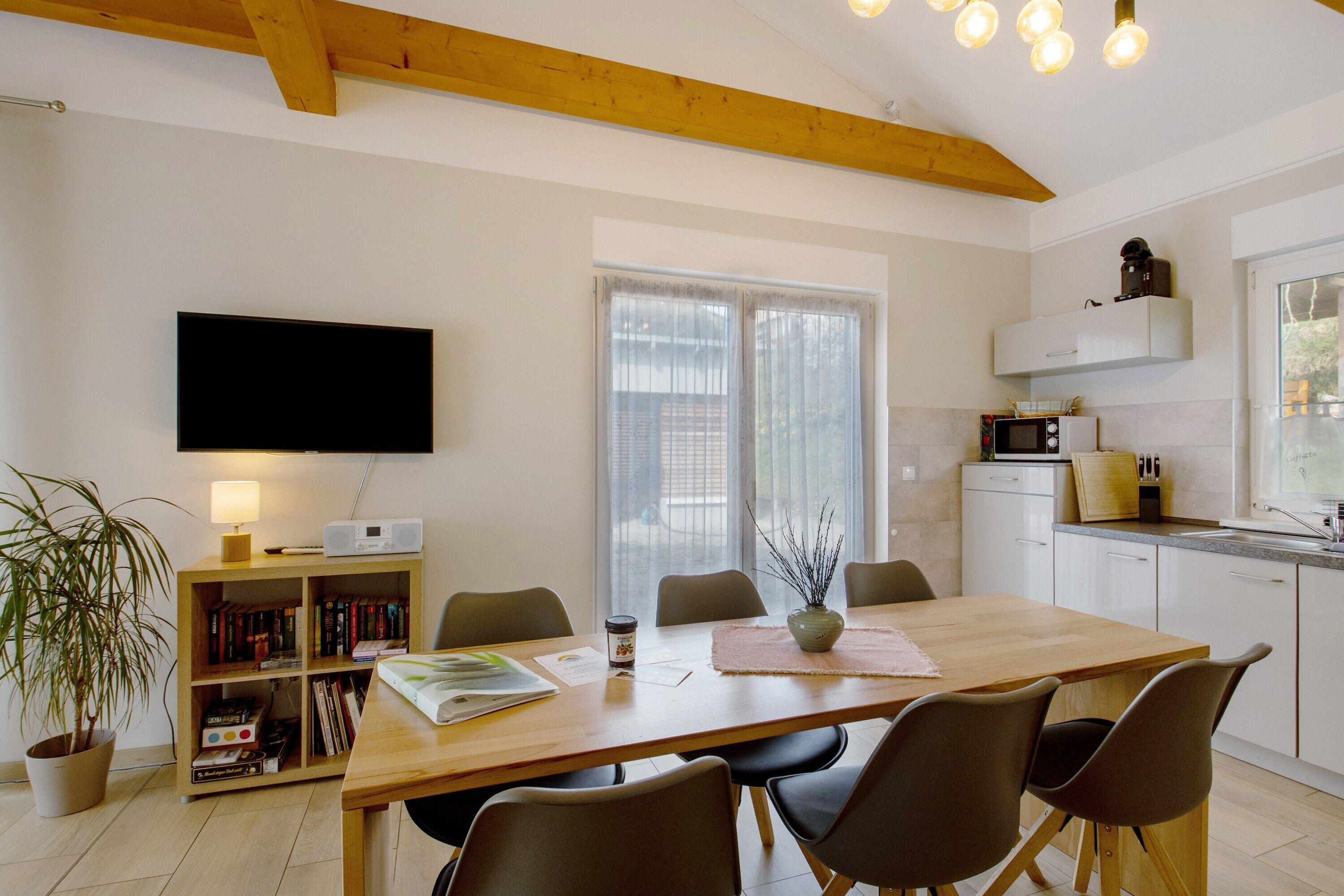 Een moderne keuken met een houten tafel, stoelen, een flatscreen televisie, een boekenkast en een potplant.